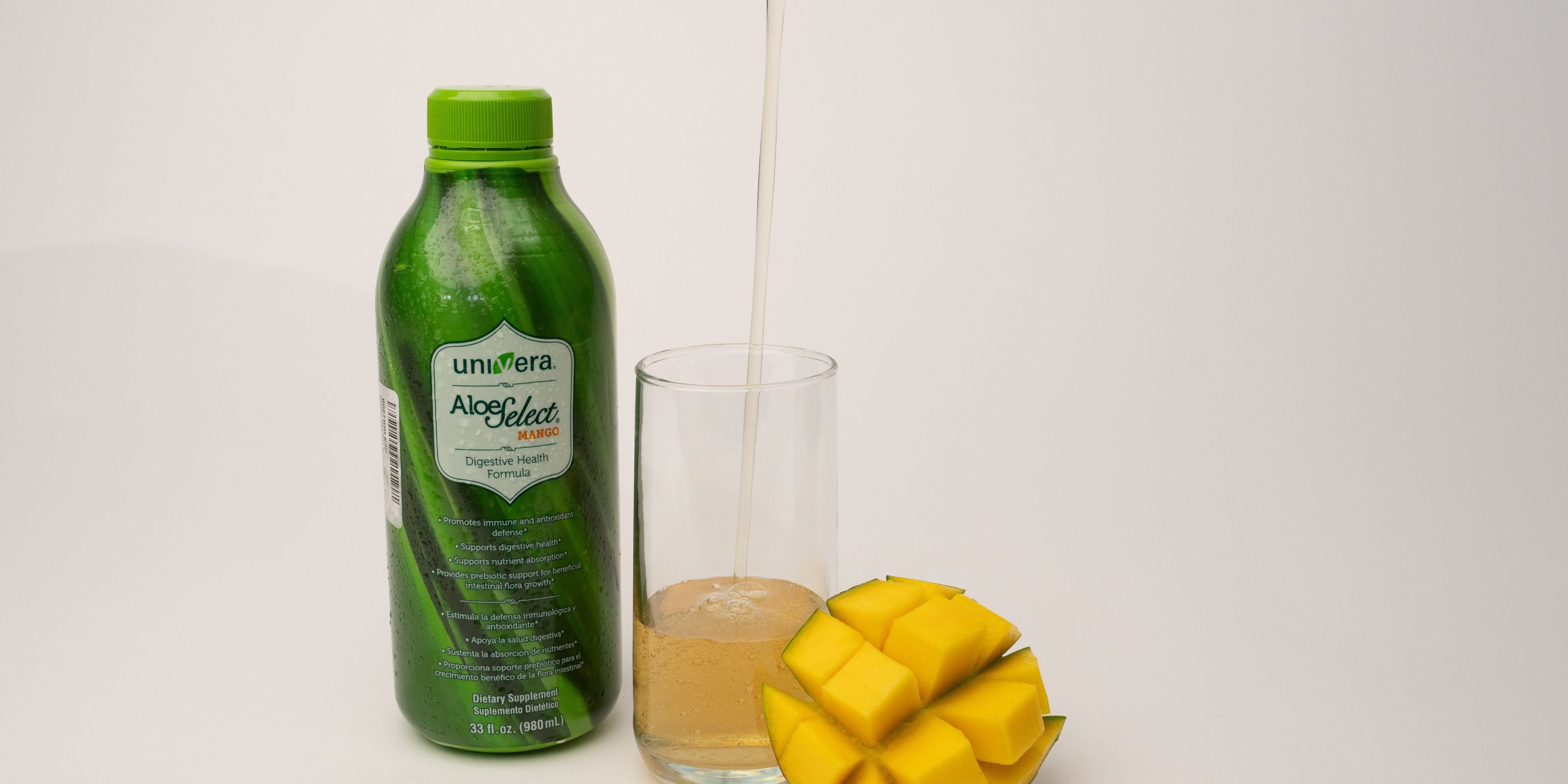 Univera Aloe Vera juice bottle with a glass of Aloe Select Mango and a sliced mango on a white background